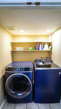Washroom with washing machine and dryer and tile patterned flooring