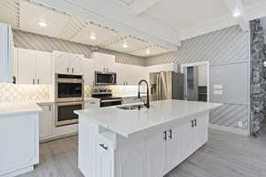 Kitchen with stainless steel appliances, a sink, tasteful backsplash, light countertops, and beamed ceiling