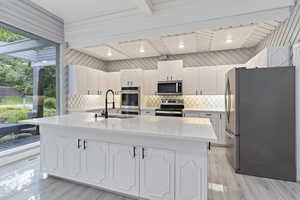 Kitchen with appliances with stainless steel finishes, a sink, white cabinets, backsplash, and light countertops
