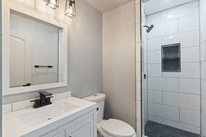 Full bath featuring toilet, tiled shower, and vanity