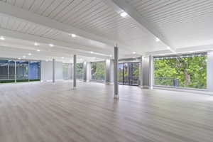 Unfurnished living room featuring beam ceiling, wood finished floors, baseboards, and healthy amount of natural light
