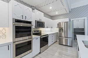 Kitchen featuring appliances with stainless steel finishes, backsplash, and white cabinetry
