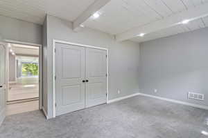 Unfurnished bedroom featuring carpet, a closet, baseboards, and wooden ceiling with exposed beams