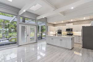 Kitchen with stainless steel appliances, a skylight, white cabinetry, plenty of natural light, and beamed ceiling