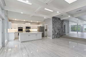Kitchen with appliances with stainless steel finishes, light countertops, tasteful backsplash, beam ceiling, and an island with sink