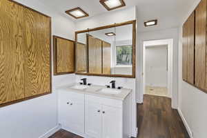 Full bathroom featuring double vanity, wood finished floors, and baseboards