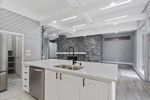 Kitchen featuring appliances with stainless steel finishes, a sink, white cabinetry, beamed ceiling, and light wood-style flooring