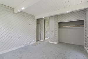 Unfurnished bedroom with carpet, a closet, baseboards, wooden ceiling with exposed beams, and wood walls
