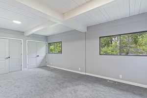 Unfurnished bedroom with beamed ceiling, carpet floors, baseboards, and two closets