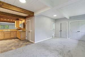 Kitchen featuring carpet, beam ceiling, light brown cabinetry, baseboards, and a sink