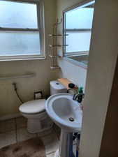 Bathroom with healthy amount of natural light, toilet, tile patterned floors, and a sink