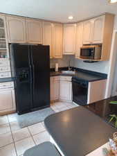 Kitchen with black appliances, a sink, dark countertops, light tile patterned flooring, and recessed lighting
