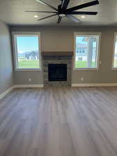 Unfurnished living room featuring wood finished floors, a fireplace, a textured ceiling, a ceiling fan, and baseboards