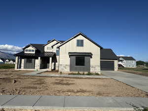 Modern farmhouse style home with a standing seam roof, concrete driveway, metal roof, an attached garage, and stone siding