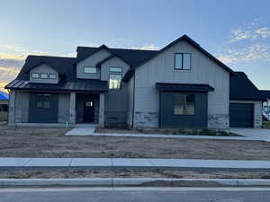 Modern farmhouse style home with a standing seam roof, stone siding, board and batten siding, covered porch, and metal roof