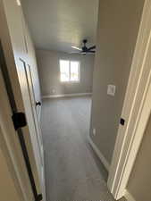 Empty room with a textured ceiling, baseboards, carpet floors, and ceiling fan