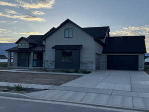 Modern inspired farmhouse with stone siding, a standing seam roof, driveway, board and batten siding, and a garage