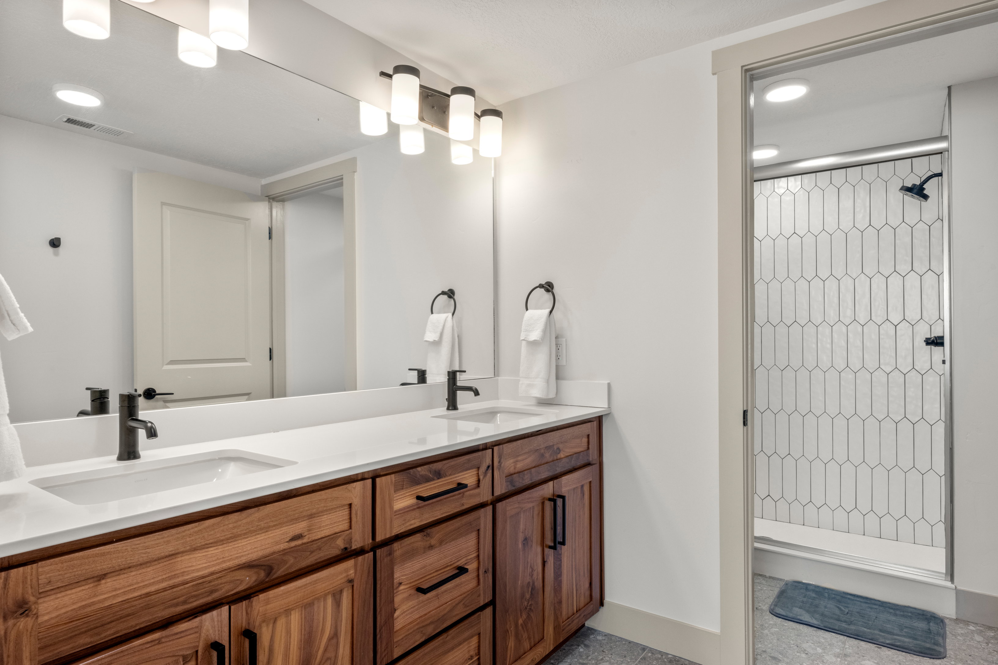 Full bathroom featuring tiled shower, double vanity, baseboards, and recessed lighting