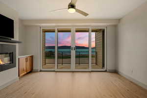 Unfurnished living room featuring light wood-type flooring, a glass covered fireplace, a ceiling fan, and baseboards