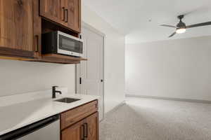Kitchen featuring stainless steel appliances, light carpet, a sink, light countertops, and ceiling fan