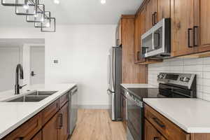 Kitchen featuring stainless steel appliances, a sink, light wood-style floors, brown cabinets, and recessed lighting
