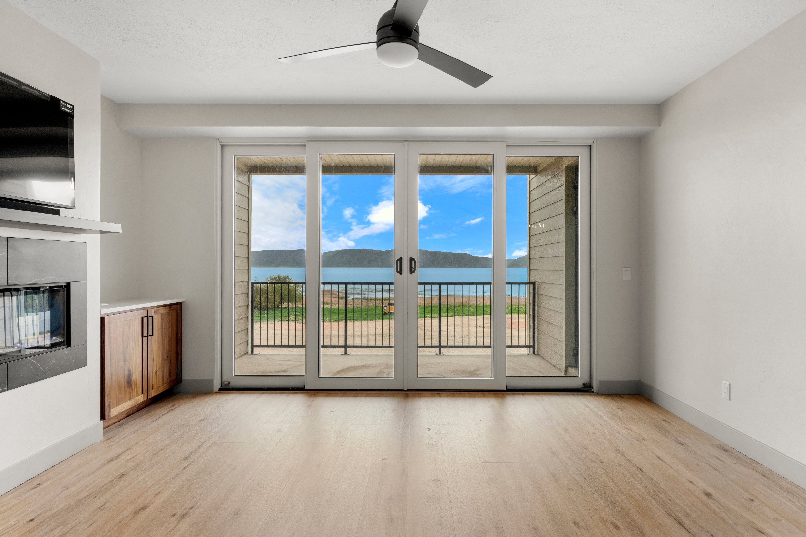 Unfurnished living room with light wood finished floors, a ceiling fan, a glass covered fireplace, and baseboards