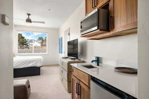 Kitchen with stainless steel dishwasher, brown cabinets, light colored carpet, light countertops, and a sink