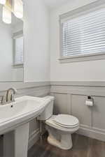 Half bath with wood finished floors, toilet, a sink, and a wainscoted wall