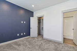 Unfurnished bedroom featuring carpet flooring, baseboards, a spacious closet, recessed lighting, and ensuite bath