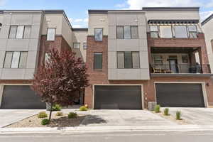 Townhome / multi-family property featuring a garage, driveway, cooling unit, stucco siding, and brick siding