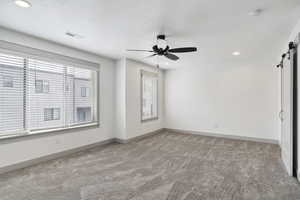 Empty room featuring a barn door, light carpet, ceiling fan, a smoke detector, and recessed lighting