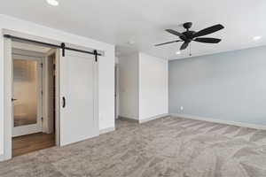 Unfurnished bedroom with carpet flooring, a barn door, recessed lighting, baseboards, and ceiling fan