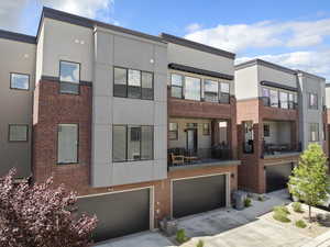 Rear view of property featuring a garage, driveway, brick siding, stucco siding, and central AC