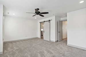 Unfurnished bedroom with carpet flooring, a barn door, recessed lighting, baseboards, and a ceiling fan
