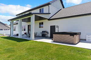 Rear view of property with a hot tub, a patio, roof with shingles, and board and batten siding