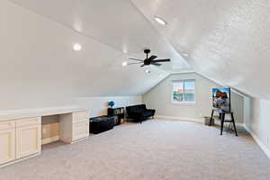 Living area featuring light colored carpet, baseboards, lofted ceiling, ceiling fan, and a textured ceiling