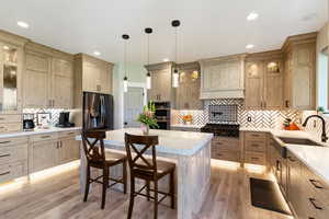 Kitchen featuring a sink, stainless steel double oven, refrigerator with ice dispenser, decorative backsplash, and light countertops