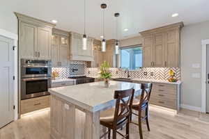 Kitchen featuring stainless steel double oven, a sink, light wood finished floors, tasteful backsplash, and recessed lighting