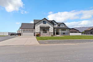 Modern farmhouse style home with a standing seam roof, stone siding, an attached garage, concrete driveway, and metal roof