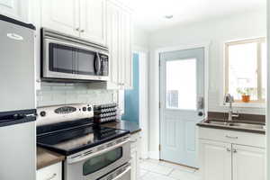 Kitchen with stainless steel appliances, a sink, dark countertops, tasteful backsplash, and white cabinetry