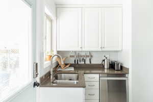 Kitchen featuring a sink, stainless steel dishwasher, decorative backsplash, white cabinets, and dark countertops