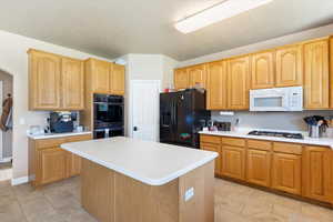 Kitchen with white appliances, light countertops, a center island, light tile patterned flooring, and arched walkways