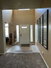 Foyer entrance featuring light tile patterned floors, arched walkways, baseboards, a towering ceiling, and light colored carpet