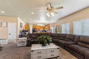 Carpeted living room featuring a textured ceiling, a chandelier, ceiling fan, and recessed lighting