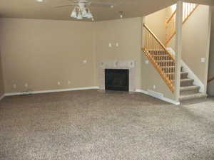 Unfurnished living room featuring stairs, ceiling fan, a tile fireplace, carpet floors, and baseboards