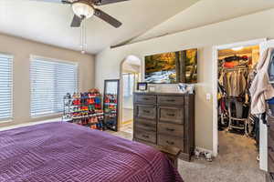 Bedroom featuring a walk in closet, lofted ceiling, light colored carpet, baseboards, and a closet