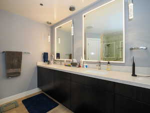 Bathroom featuring a stall shower, double vanity, baseboards, and wood finished floors