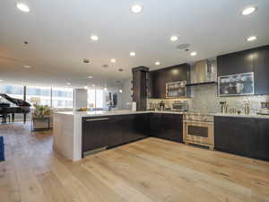 Kitchen featuring wall chimney exhaust hood, luxury range, modern cabinets, light countertops, and decorative backsplash