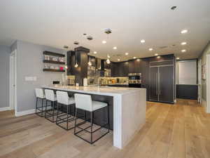 Kitchen with wall chimney exhaust hood, paneled built in refrigerator, a peninsula, a kitchen breakfast bar, and light wood finished floors