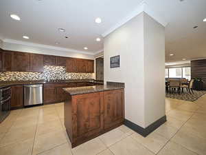 Kitchen featuring stainless steel dishwasher, backsplash, dark stone counters, a sink, and light tile patterned flooring